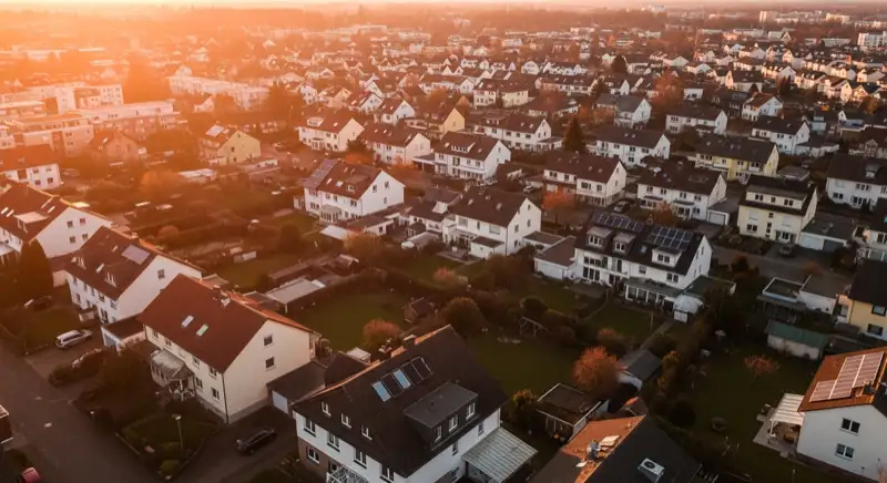 Aerial drone view of typical German residential neighborhood with mixed roof types, red and dark roof tiles, gardens visible, sunny day