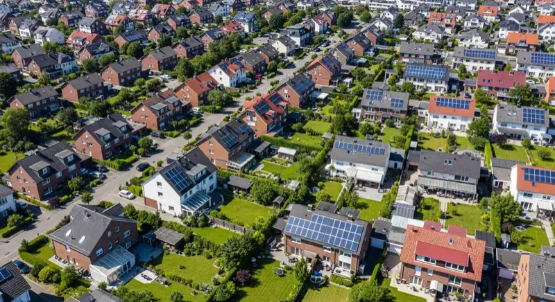 Aerial drone view of typical German residential neighborhood with mixed roof types, red and dark roof tiles, gardens visible, sunny day