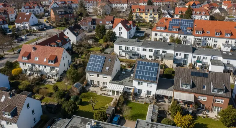 Aerial drone view of typical German residential neighborhood with mixed roof types, red and dark roof tiles, gardens visible, sunny day