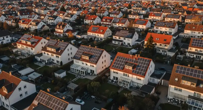 Aerial drone view of typical German residential neighborhood with mixed roof types, red and dark roof tiles, gardens visible, sunny day