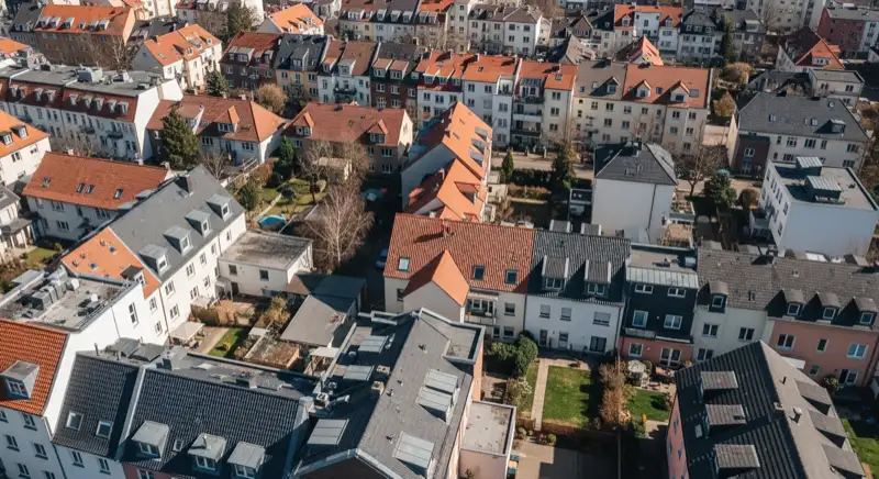 Aerial drone view of typical German residential neighborhood with mixed roof types, red and dark roof tiles, gardens visible, sunny day