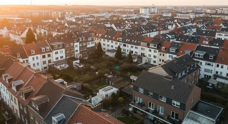 Aerial drone view of typical German residential neighborhood with mixed roof types, red and dark roof tiles, gardens visible, sunny day