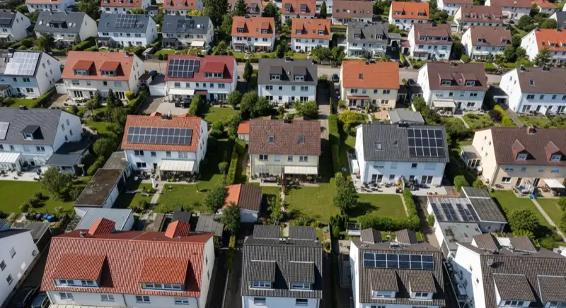 Aerial drone view of typical German residential neighborhood with mixed roof types, red and dark roof tiles, gardens visible, sunny day