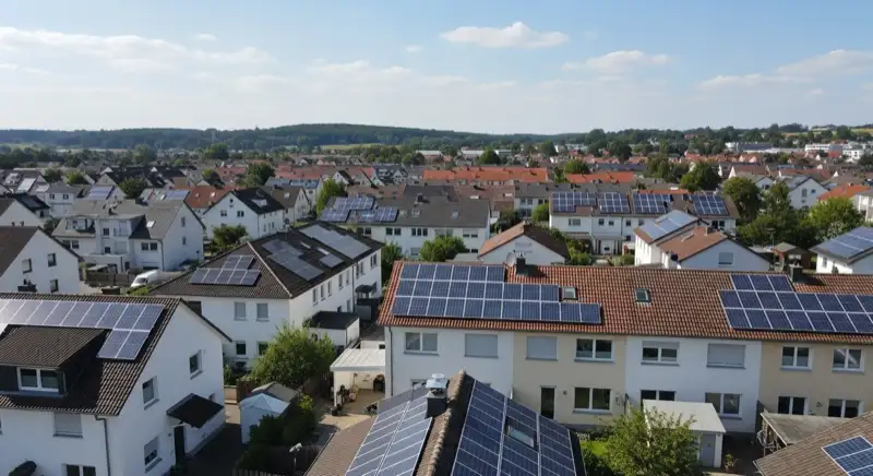 Aerial drone view of typical German residential neighborhood with mixed roof types, red and dark roof tiles, gardens visible, sunny day