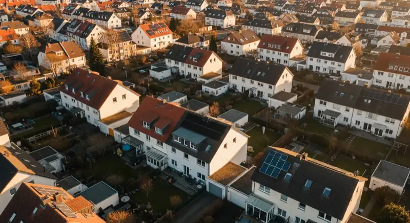 Aerial drone view of typical German residential neighborhood with mixed roof types, red and dark roof tiles, gardens visible, sunny day