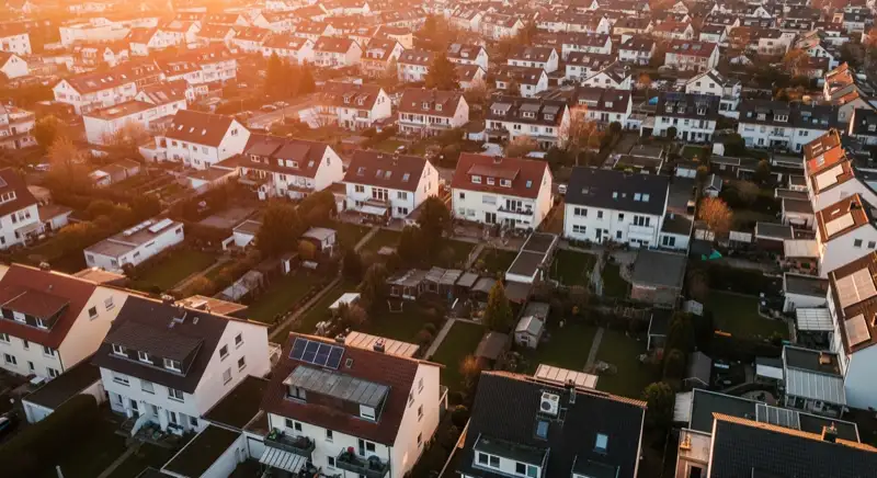 Aerial drone view of typical German residential neighborhood with mixed roof types, red and dark roof tiles, gardens visible, sunny day