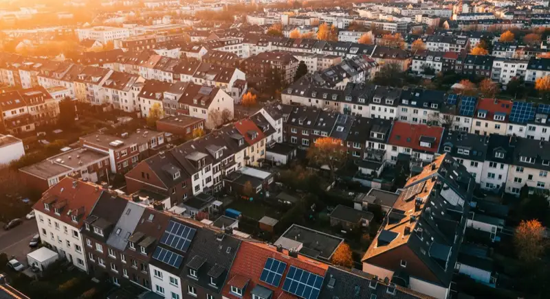 Aerial drone view of typical German residential neighborhood with mixed roof types, red and dark roof tiles, gardens visible, sunny day