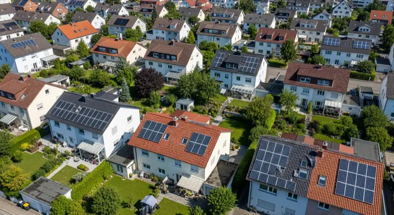 Aerial drone view of typical German residential neighborhood with mixed roof types, red and dark roof tiles, gardens visible, sunny day