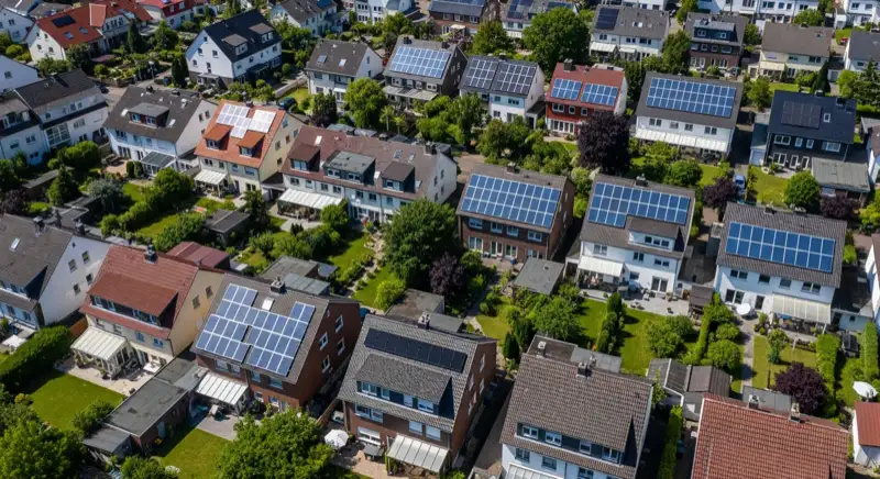 Aerial drone view of typical German residential neighborhood with mixed roof types, red and dark roof tiles, gardens visible, sunny day
