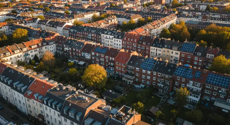 Aerial drone view of typical German residential neighborhood with mixed roof types, red and dark roof tiles, gardens visible, sunny day