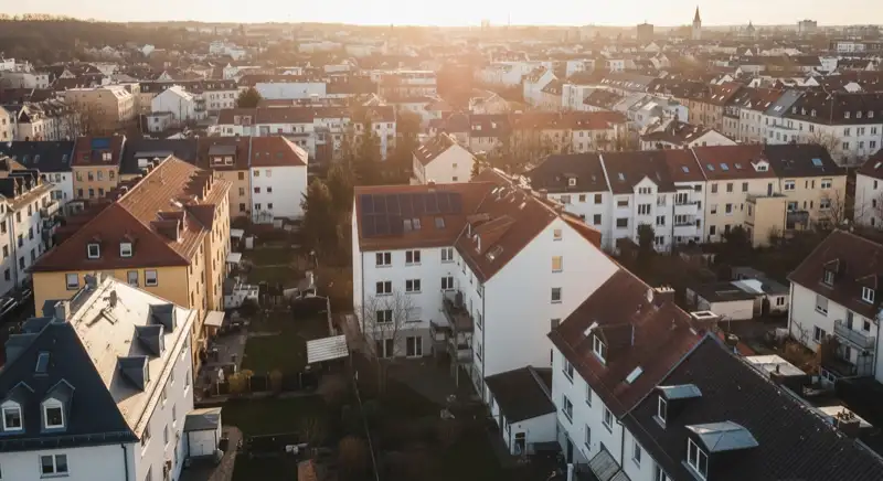 Aerial drone view of typical German residential neighborhood with mixed roof types, red and dark roof tiles, gardens visible, sunny day