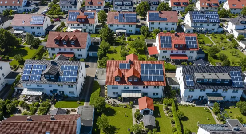 Aerial drone view of typical German residential neighborhood with mixed roof types, red and dark roof tiles, gardens visible, sunny day