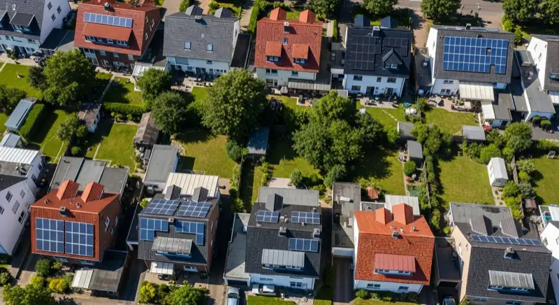 Aerial drone view of typical German residential neighborhood with mixed roof types, red and dark roof tiles, gardens visible, sunny day