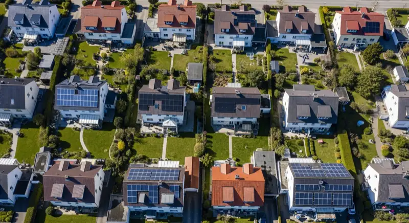 Aerial drone view of typical German residential neighborhood with mixed roof types, red and dark roof tiles, gardens visible, sunny day