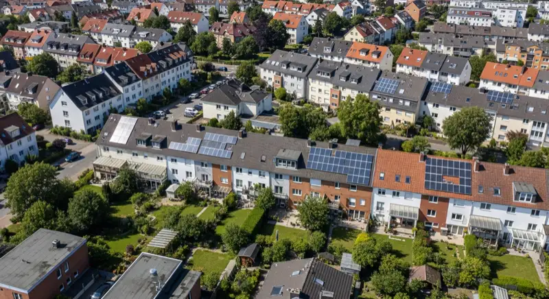 Aerial drone view of typical German residential neighborhood with mixed roof types, red and dark roof tiles, gardens visible, sunny day