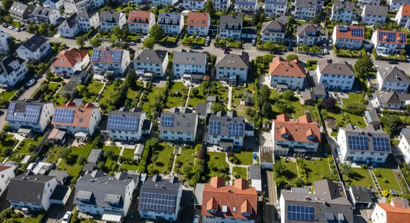 Aerial drone view of typical German residential neighborhood with mixed roof types, red and dark roof tiles, gardens visible, sunny day