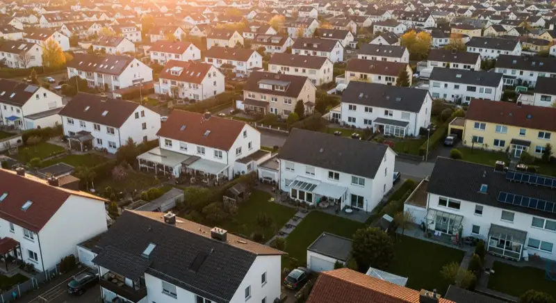 Aerial drone view of typical German residential neighborhood with mixed roof types, red and dark roof tiles, gardens visible, sunny day