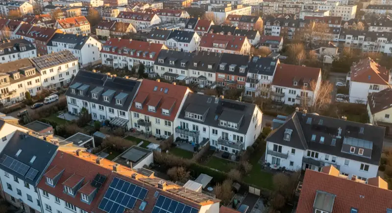 Aerial drone view of typical German residential neighborhood with mixed roof types, red and dark roof tiles, gardens visible, sunny day