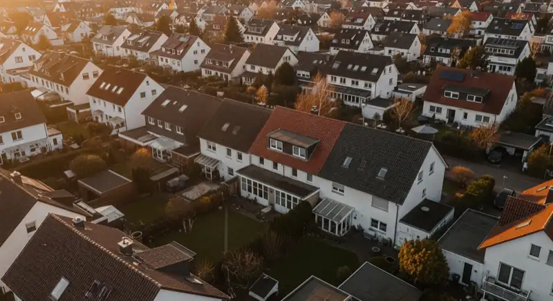 Aerial drone view of typical German residential neighborhood with mixed roof types, red and dark roof tiles, gardens visible, sunny day