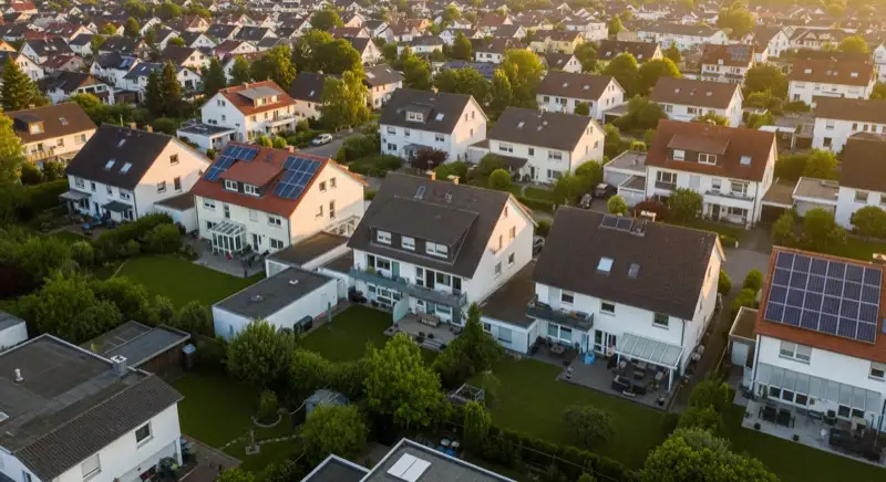 Aerial drone view of typical German residential neighborhood with mixed roof types, red and dark roof tiles, gardens visible, sunny day