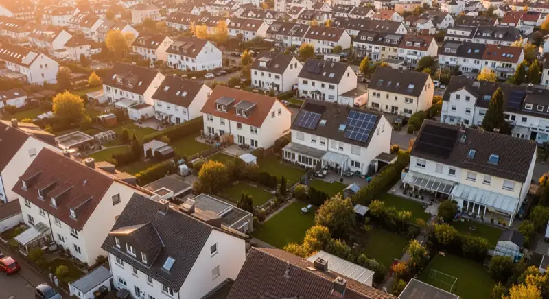 Aerial drone view of typical German residential neighborhood with mixed roof types, red and dark roof tiles, gardens visible, sunny day
