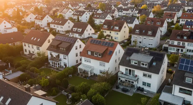 Aerial drone view of typical German residential neighborhood with mixed roof types, red and dark roof tiles, gardens visible, sunny day