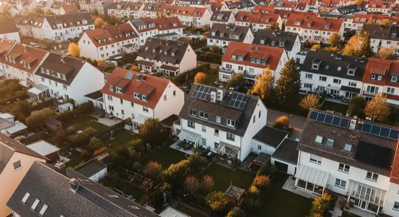 Aerial drone view of typical German residential neighborhood with mixed roof types, red and dark roof tiles, gardens visible, sunny day