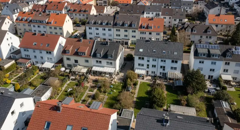 Aerial drone view of typical German residential neighborhood with mixed roof types, red and dark roof tiles, gardens visible, sunny day