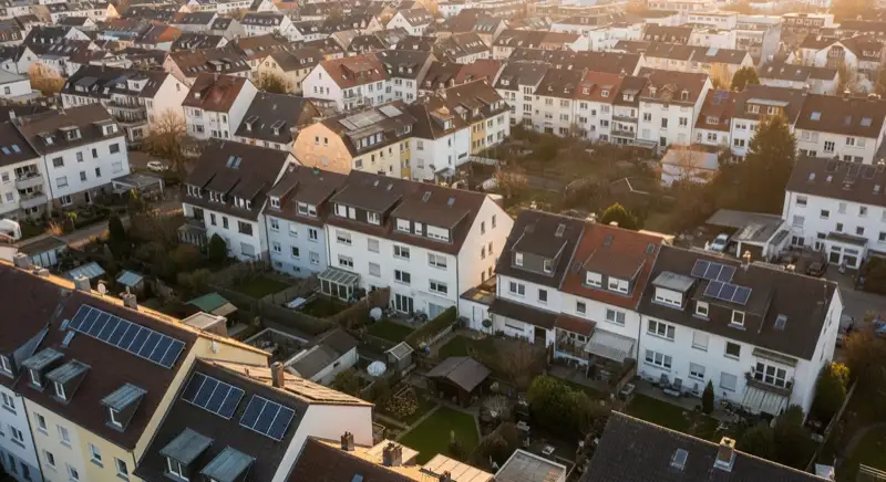 Aerial drone view of typical German residential neighborhood with mixed roof types, red and dark roof tiles, gardens visible, sunny day