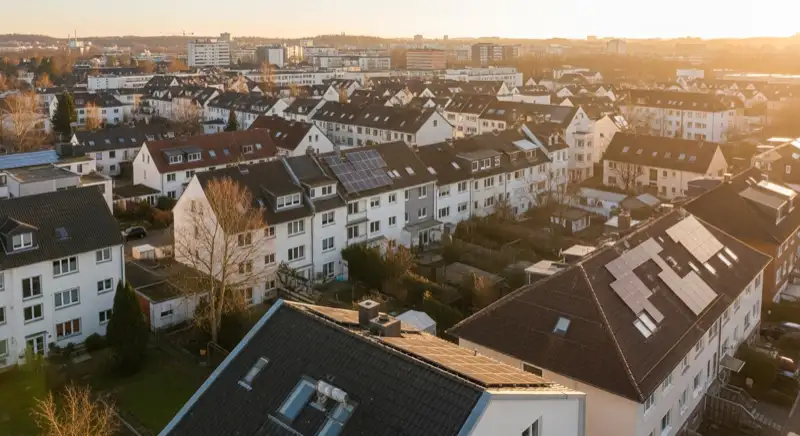 Aerial drone view of typical German residential neighborhood with mixed roof types, red and dark roof tiles, gardens visible, sunny day