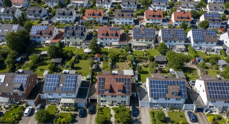 Aerial drone view of typical German residential neighborhood with mixed roof types, red and dark roof tiles, gardens visible, sunny day