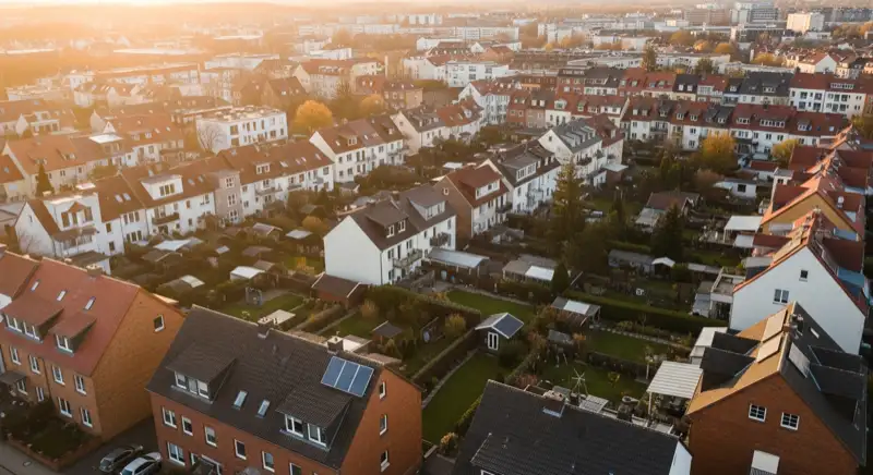 Aerial drone view of typical German residential neighborhood with mixed roof types, red and dark roof tiles, gardens visible, sunny day