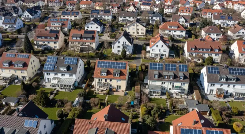 Aerial drone view of typical German residential neighborhood with mixed roof types, red and dark roof tiles, gardens visible, sunny day
