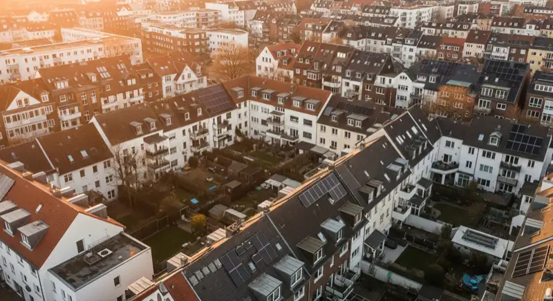 Aerial drone view of typical German residential neighborhood with mixed roof types, red and dark roof tiles, gardens visible, sunny day