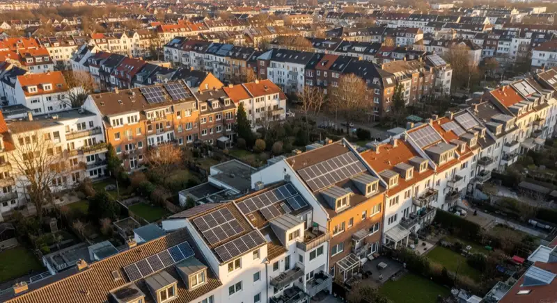 Aerial drone view of typical German residential neighborhood with mixed roof types, red and dark roof tiles, gardens visible, sunny day