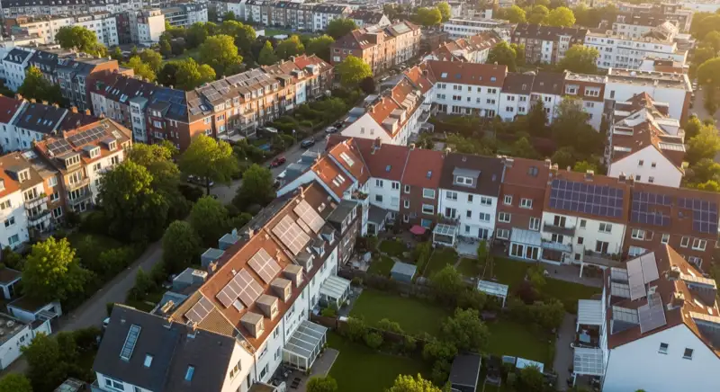 Aerial drone view of typical German residential neighborhood with mixed roof types, red and dark roof tiles, gardens visible, sunny day