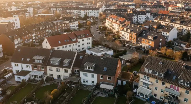 Aerial drone view of typical German residential neighborhood with mixed roof types, red and dark roof tiles, gardens visible, sunny day