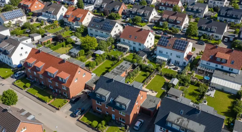 Aerial drone view of typical German residential neighborhood with mixed roof types, red and dark roof tiles, gardens visible, sunny day