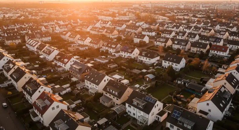 Aerial drone view of typical German residential neighborhood with mixed roof types, red and dark roof tiles, gardens visible, sunny day