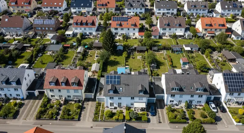 Aerial drone view of typical German residential neighborhood with mixed roof types, red and dark roof tiles, gardens visible, sunny day