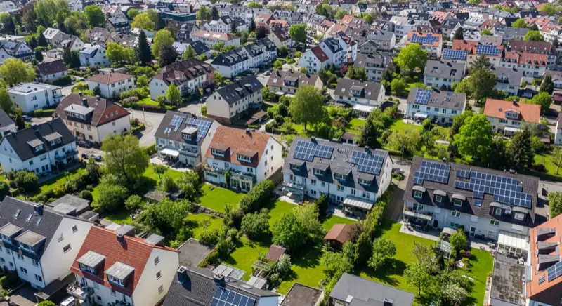 Aerial drone view of typical German residential neighborhood with mixed roof types, red and dark roof tiles, gardens visible, sunny day