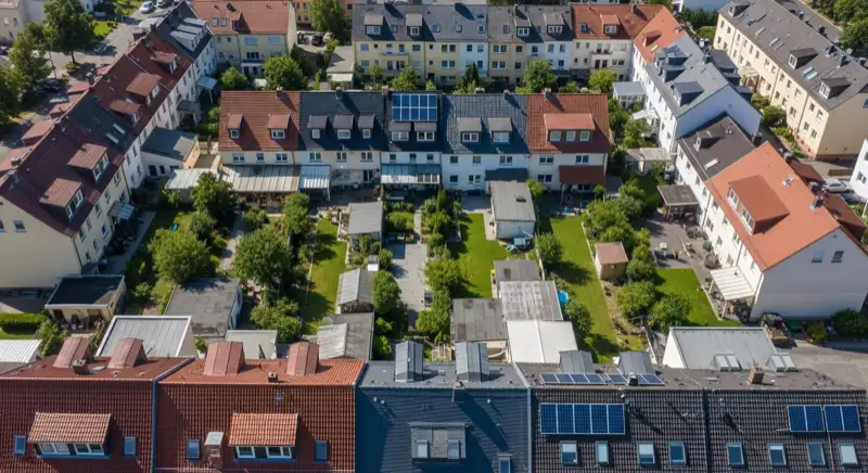 Aerial drone view of typical German residential neighborhood with mixed roof types, red and dark roof tiles, gardens visible, sunny day