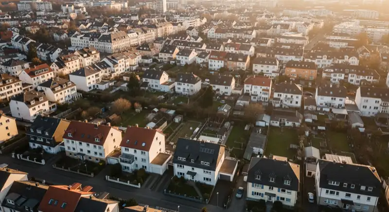 Aerial drone view of typical German residential neighborhood with mixed roof types, red and dark roof tiles, gardens visible, sunny day