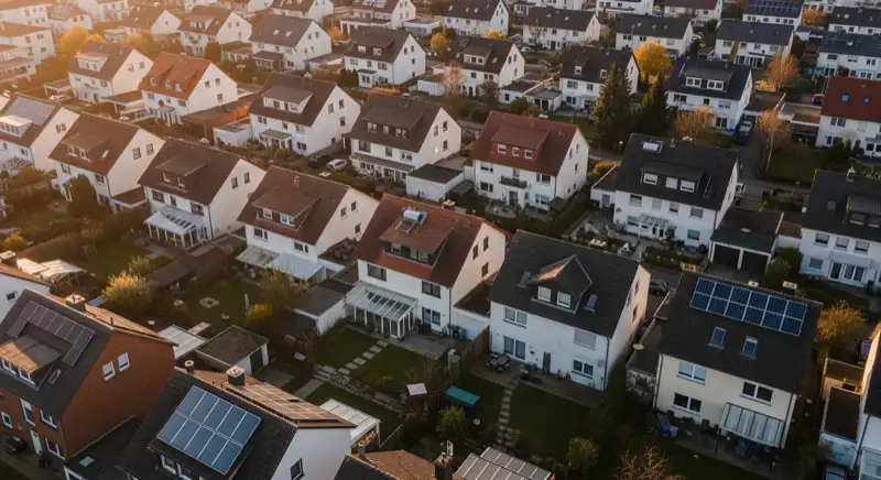 Aerial drone view of typical German residential neighborhood with mixed roof types, red and dark roof tiles, gardens visible, sunny day