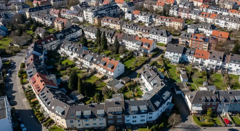 Aerial drone view of typical German residential neighborhood with mixed roof types, red and dark roof tiles, gardens visible, sunny day