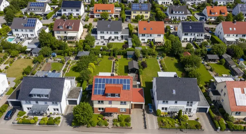 Aerial drone view of typical German residential neighborhood with mixed roof types, red and dark roof tiles, gardens visible, sunny day