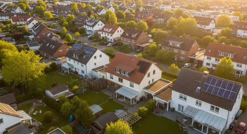 Aerial drone view of typical German residential neighborhood with mixed roof types, red and dark roof tiles, gardens visible, sunny day