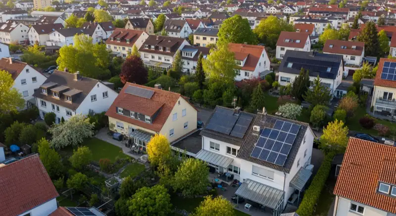 Aerial drone view of typical German residential neighborhood with mixed roof types, red and dark roof tiles, gardens visible, sunny day