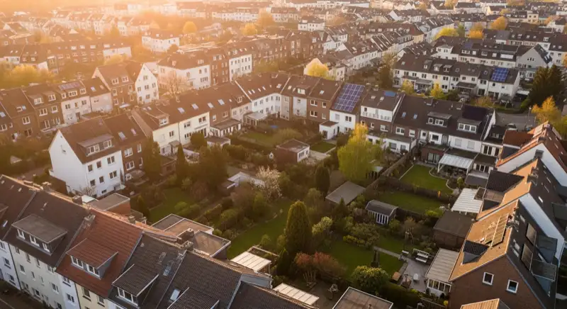 Aerial drone view of typical German residential neighborhood with mixed roof types, red and dark roof tiles, gardens visible, sunny day