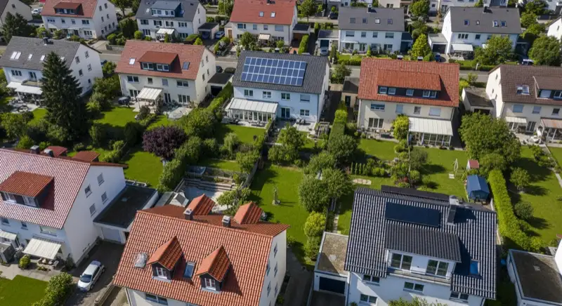 Aerial drone view of typical German residential neighborhood with mixed roof types, red and dark roof tiles, gardens visible, sunny day